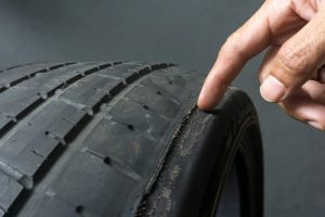 Finger pointing to damage on tire tread. Tire tread problems by tire pressure improper, Wheel alignment
